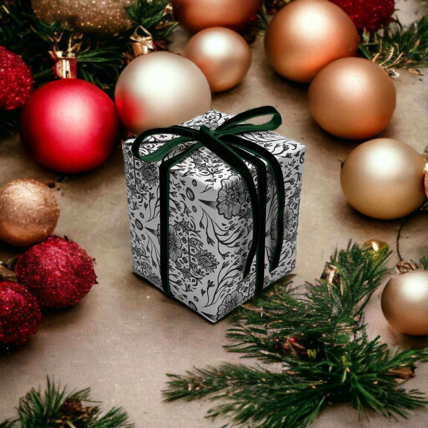 AEMBR holiday gift box with floral wrapping and black ribbon, surrounded by ornaments and pine.