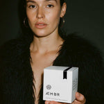 Woman in black faux fur coat holding AEMBR luxury coconut wax candle box