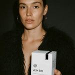 Woman in faux fur coat holding AEMBR luxury coconut wax candle box, black background