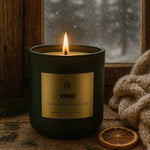 AEMBR Hygge scented candle burning by a snowy window, with knit blanket and dried orange slice