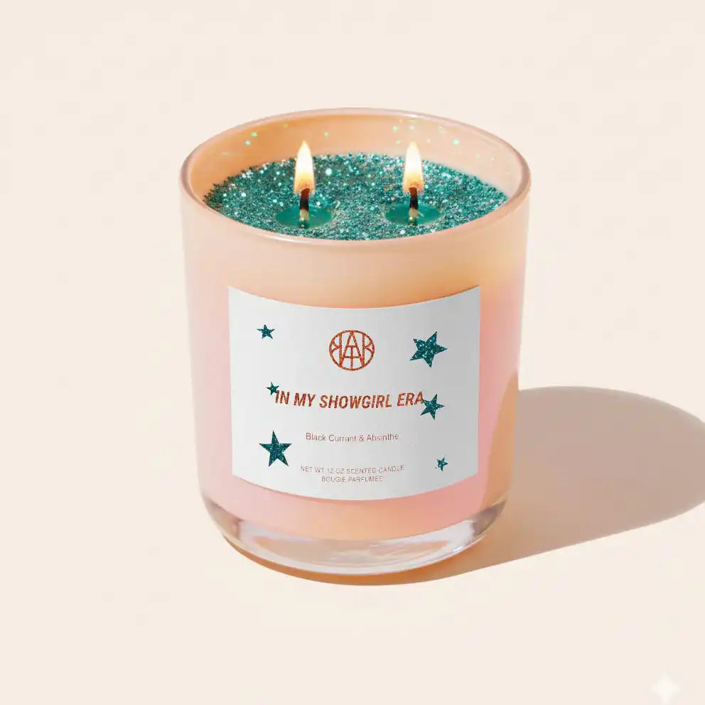 AEMBR In My Showgirl Era scented candle with green glitter, burning two wicks, on a neutral background.