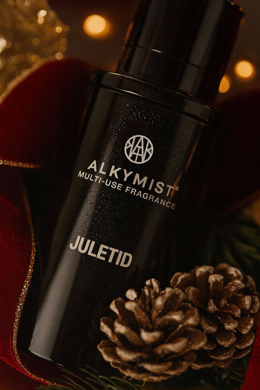 Black Alkymist Juletid multi-use fragrance bottle with pinecones on a blurred background