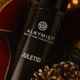 Black Alkymist Juletid multi-use fragrance bottle with pinecones on a blurred background