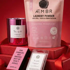 AEMBR non-toxic laundry powder, scented candle, and wax melts in pink packaging on red display.