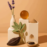 Lavender sprigs, sage, cocoa pod, powder, and amber sphere on beige blocks, AEMBR non-toxic home.