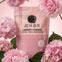 AEMBR Love Spell laundry powder in pink packaging, surrounded by cherry blossoms and green leaves.
