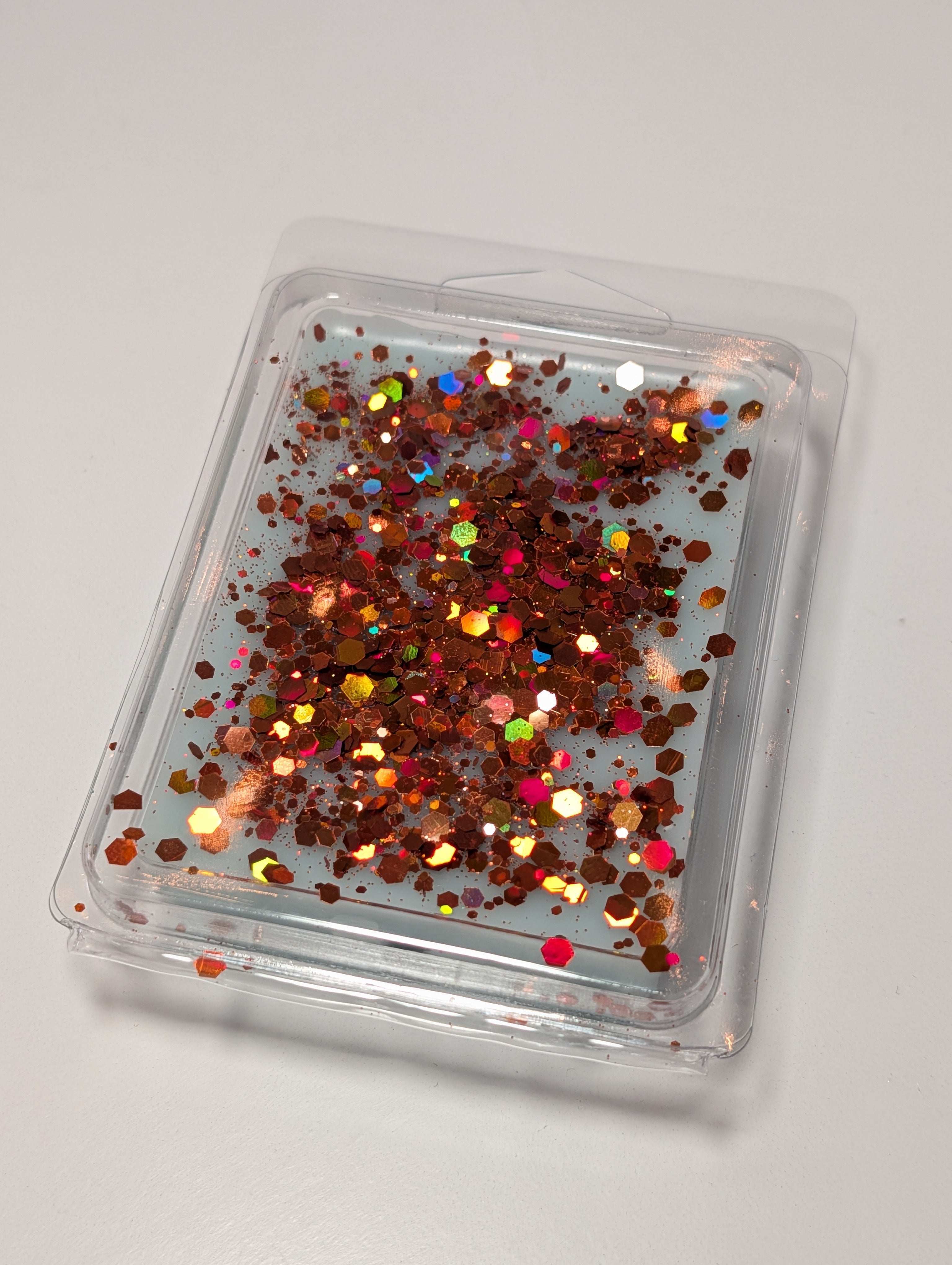 AEMBR wax melt with copper and rainbow glitter in clear clamshell packaging on white surface