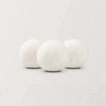Three white wool dryer balls by AEMBR on a plain background, non-toxic laundry product