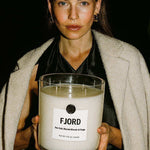 Woman holding a large FJORD candle labeled sea salt, blonde woods, and sage by AEMBR