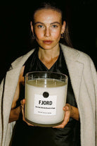 Woman holding large AEMBR FJORD candle with sea salt, blonde woods, and sage label