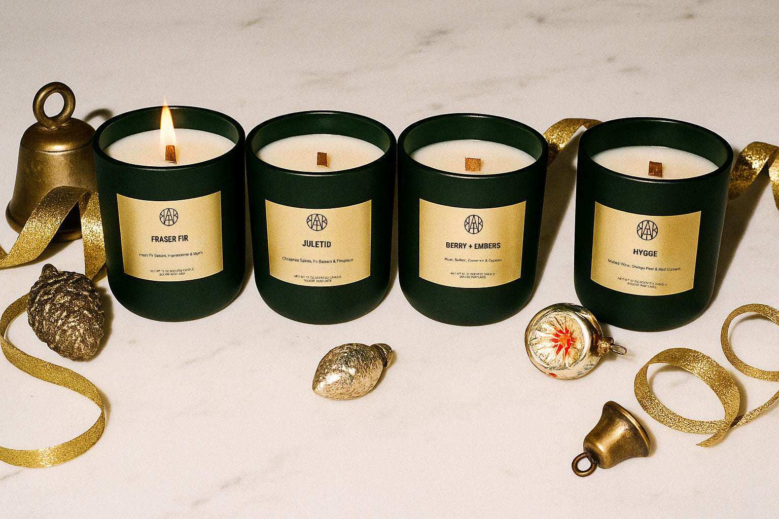 AEMBR winter collection scented candles in dark green jars with gold labels, decorated with festive ornaments and ribbon.