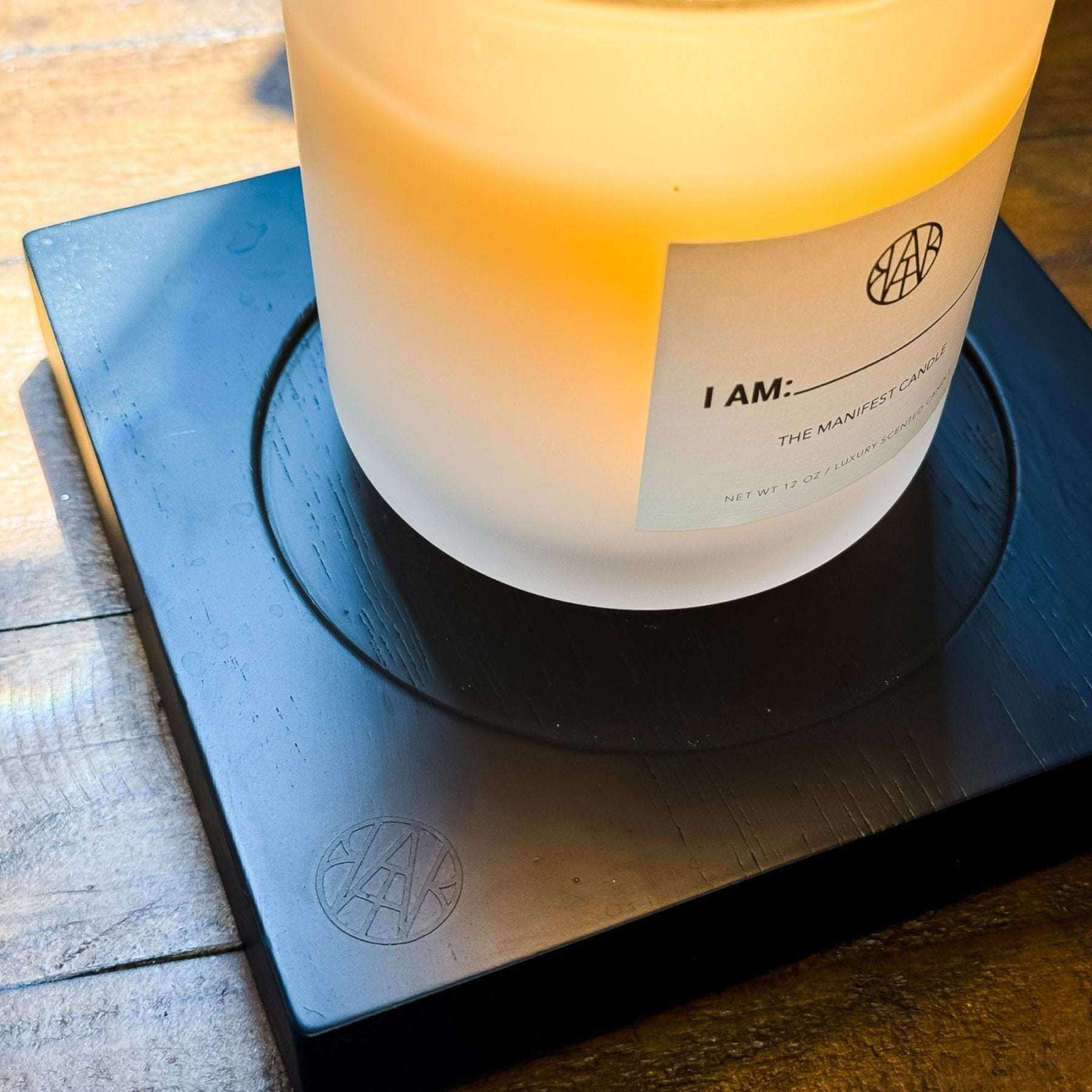 AEMBR frosted glass candle with wooden wick on black coaster, warm light, wooden table