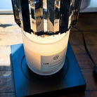 AEMBR frosted glass candle with wooden wick on a wooden table, under a modern lamp.